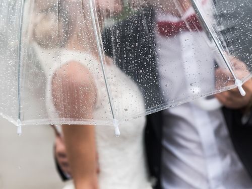 the bride and groom in the rain are covered with a transparent umbrella rain drops
